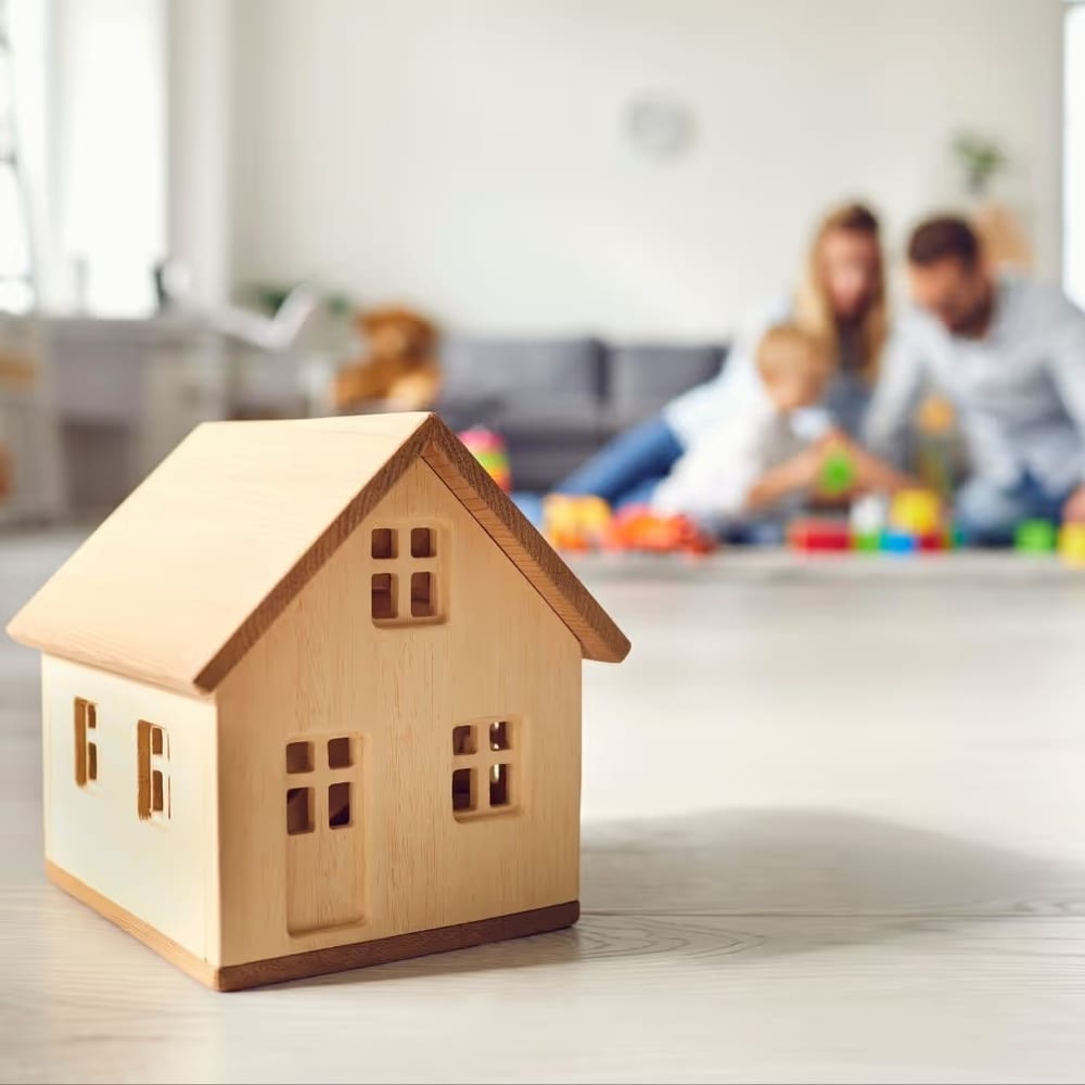 Maquete de casa em primeiro plano e família brincando ao fundo